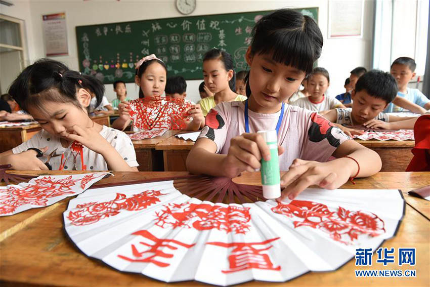 先生の指導(dǎo)のもと、「切り絵扇子」を作る山東省臨沂市沂南経済開発區(qū)実験學(xué)校の生徒たち（6月20日、撮影?杜昱葆）。