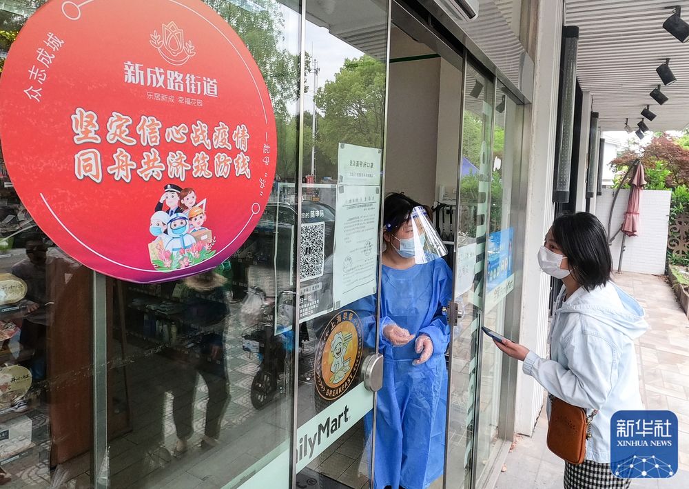 上海市嘉定區(qū)新成路街道（エリア）でQRコードをスキャンしてコンビニに入店する人（寫真右）。同エリアではコロナ感染対策基準を満たすと認定された商店などに赤い円形のシールを掲示している（5月9日撮影）。