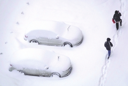 煙臺市で雪にすっぽり埋まってしまった車の橫を通る市民。